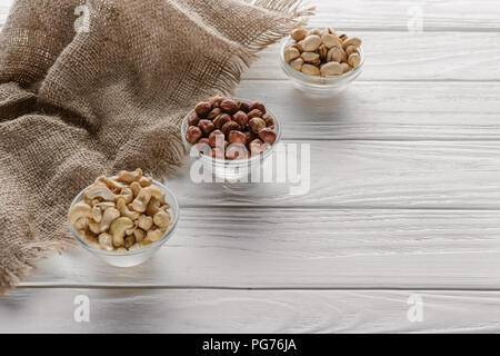 organic nuts in glass bowls on white wooden background Stock Photo