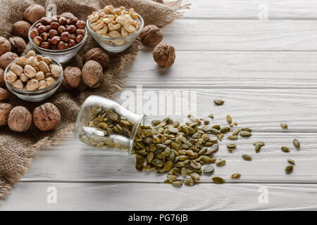 various nuts in glass bowls and pumpkin seeds in jar on white wooden surface Stock Photo