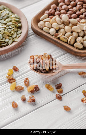 mixed nuts in plates and raisins in spoon on white wooden table Stock Photo