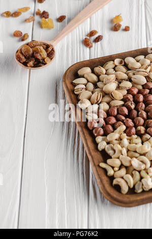 mix of nuts in plate and raisins in spoon on white wooden tabletop Stock Photo