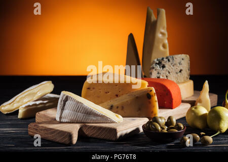 different types of appetizing cheeses on cutting board on orange Stock Photo