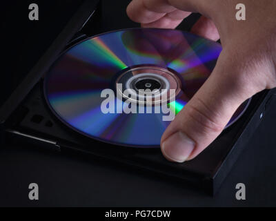 A shiny and new DVD or CD disc is shown being loaded by hand into an optical media player in a closeup view. Stock Photo
