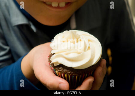 Child holding homemade cupcake with swirled frosting - USA Stock Photo