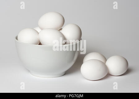 White eggs in a china bowl with three lying alongside all on a white background Stock Photo