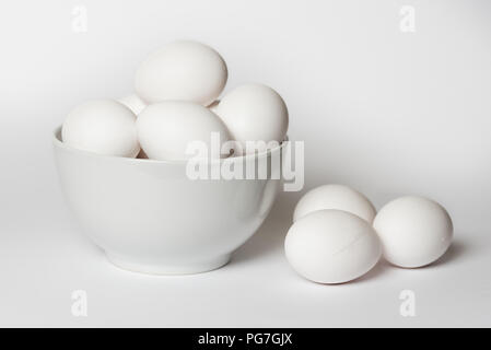 White eggs in a china bowl with three lying alongside all on a white background Stock Photo