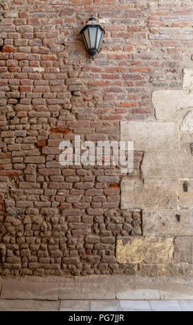 Front view of grunge weathered uneven red stone bricks wall and one lantern, Medieval Cairo, Egypt Stock Photo