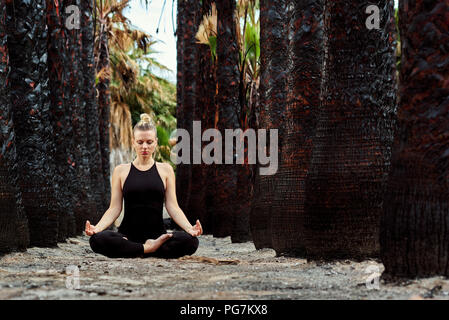 Young woman in black sportswear sitting in lotus position and meditating outdoors. Woman in early gestation. Pre natal exercising, healthy lifestyle.  Stock Photo