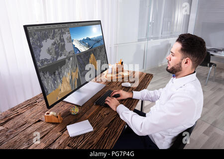 Young Man Editing 3D Landscape On Computer Over Wooden Desk Stock Photo