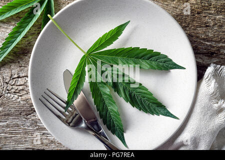 Conceptual image of a cannabis leaf on a plate with a knife and fork. Stock Photo