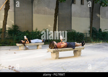 Book reading in park - Two women lying down on benches, reading books in Paris, France, Europe. Stock Photo