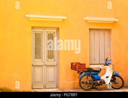 An old scooter leaning against an old peach colored wall Stock Photo