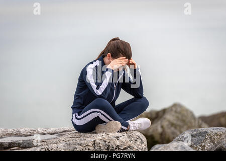 woman sitting crossed legged on rocks with her head in her hands Stock Photo