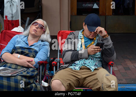 Two exhibitors, one sleeping and the other using his smartphone, sit near their booth at an outdoor art show in Santa Fe, New Mexico. Stock Photo