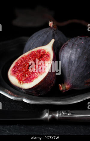 Close-up on fresh figs on dark slate stone and vintage metal plate, side view Stock Photo