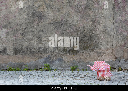 Origami elephant on cobblestones, concrete wall Stock Photo