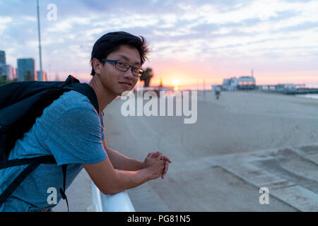 Young Chinese man with backpack looking at beach Stock Photo