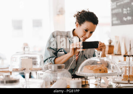 Woman taking pictures of cakes in coffee shop with her smartphone Stock Photo