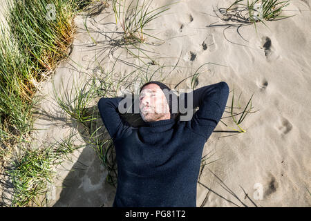 Man wearing woolly hat lying in beach dune Stock Photo