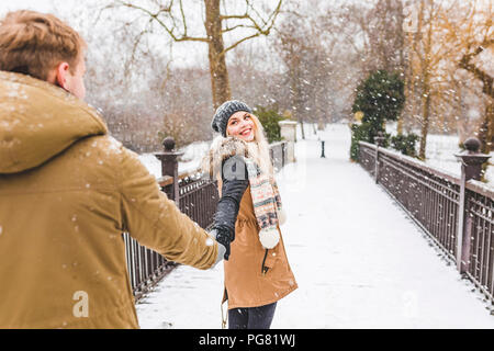 Portrait of happy teenage girl standing hand in hand with her boyfriend on footbridge on a snowy day Stock Photo