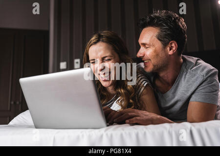 Happy couple lying on bed at home having fun with laptop Stock Photo
