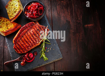 Beefsteak with rosemary, red wine onions and garlic bread on slate