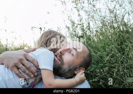 Father and little daughter lying together on a meadow hugging each other Stock Photo