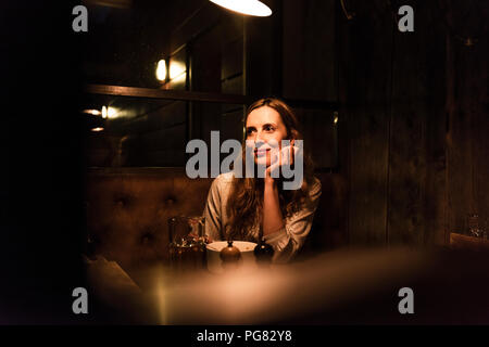 Smiling woman sitting at dining table looking sideways Stock Photo
