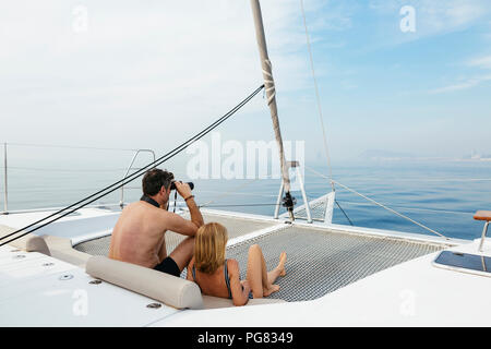 Mature couple sitting on catamaran trampoline, using binoculars Stock Photo