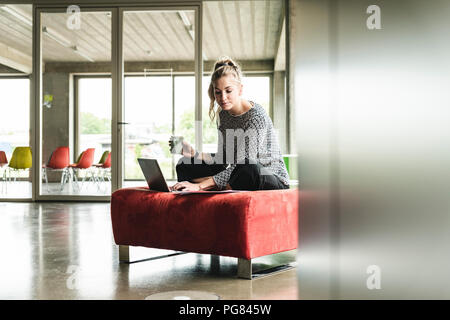 young businesswoman working in modern office, sitting on stool, using laptop Stock Photo