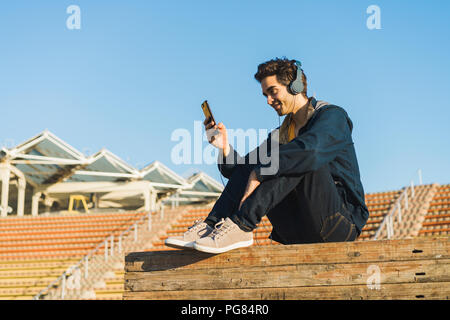 Man with headphones sitting on wood stack, using smartphone Stock Photo
