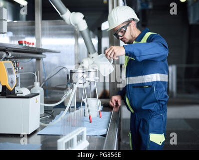 Rumania, woodworking, worker with protective workwear and measuring beaker Stock Photo