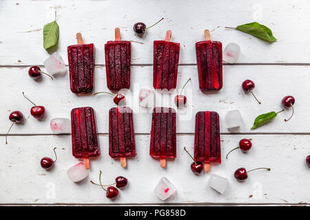 Homemade cherry ice lollies, ice cubes and cherries on white wood Stock Photo