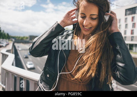 Smiling young woman listening to music on motorway bridge Stock Photo
