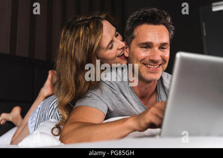 Happy couple lying on bed at home with laptop Stock Photo