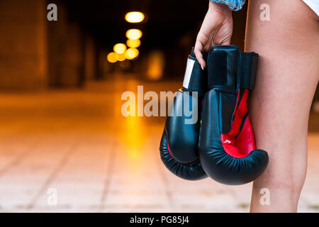 Close-up of woman holding boxing gloves at illuminated underpass Stock Photo