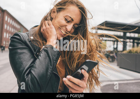 Happy young woman with windswept hair using cell phone in the city Stock Photo