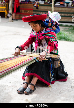 Quechua woman weaving textiles and carrying her baby Stock Photo