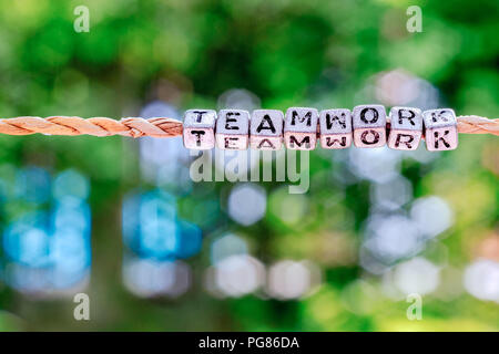 Teamwork word hanging by rope with beautiful green nature bokeh background with vintage retro tone. Cooperation, togetherness, partnership concept. Stock Photo