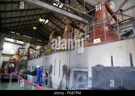 Hokkaido Asahi Beer Factory, Sapporo, Hokkaido, Japan.  A worker putting charcoal into the kiln with the impressive stills looming above. Stock Photo