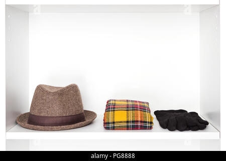 Fashion accessories storage in dressing room. Narrow brim trilby hat, plaid scarf, black gloves on white shelf inside closet. Copy space Stock Photo