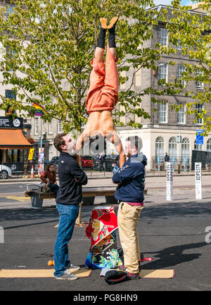Edinburgh Fringe Festival,, Edinburgh, Scotland, UK. 24th August 2018.  The sun shines on Fringe goers in Bristo Square. A Japanese street performer in Bristo Square with members of the audience participating in an acrobatic stunt Stock Photo
