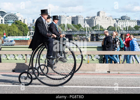 Three penny farthing cyclists ride across Westminster Bridge, London, UK. Gentlemen riders dressed in period costume. Penny farthings by UDC penny farthings, Unicycle Dot Com Stock Photo