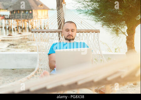 A man resting in an exotic country and working remotely on his laptop. Stock Photo