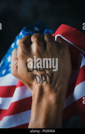 closeup of the raised fist of a young man with the text labor day handwritten in it, and the flag of the United States Stock Photo