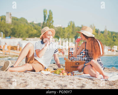 Young couple spending time on date together on the beach. Boyfriend and girlfriend on picnic. They relaxing, drinking, love each other. Relationship c Stock Photo