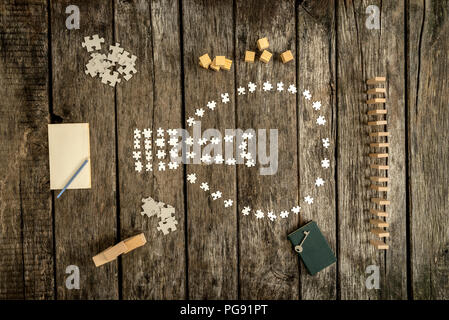 Various white puzzle pieces formed in shapes on table alongside blocks, cubes, notepad and key. Stock Photo