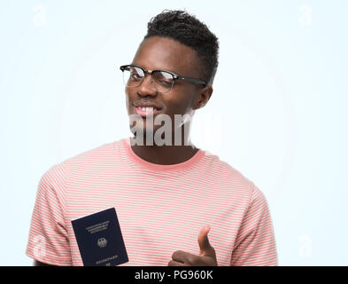 Young african american man holding german passport happy with big smile doing ok sign, thumb up with fingers, excellent sign Stock Photo