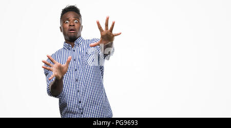 Young african american man wearing blue shirt afraid and terrified with fear expression stop gesture with hands, shouting in shock. Panic concept. Stock Photo