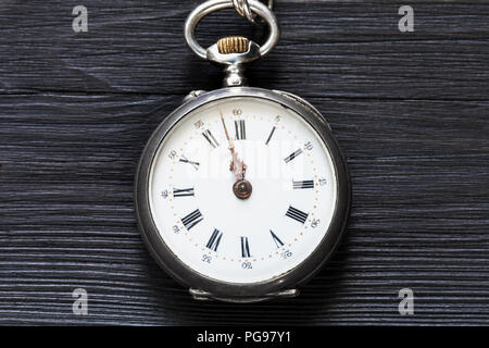 two minutes to twelve o'clock on vintage pocket watch on black wooden background Stock Photo