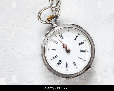 two minutes to twelve o'clock on antique pocket watch on white concrete background Stock Photo